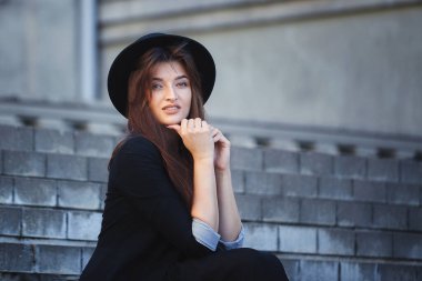 Şapkalı güzel bir kızın portresi. Hipster bir kızın görüntüsü. Şehrin etrafında yürüyüp, ön merdivenlerde poz vermek.