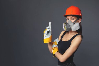Turuncu şapkalı ve koruyucu inşaat maskeli bir inşaat kızı. Zararlı gazları solumaktan ve havaya püskürtülmüş parçacıklardan korunmaya ihtiyacınız olan ağır işler için. Reklamcılık konsepti