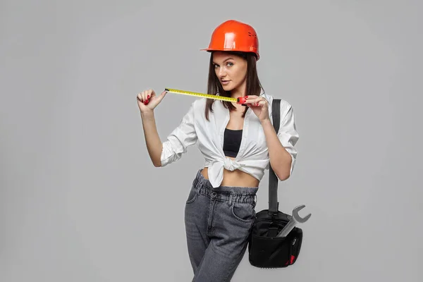 一个戴着橙色建筑头盔 头戴测量带 头戴手提包的女孩 她用白色背景描绘了一个工人 — 图库照片