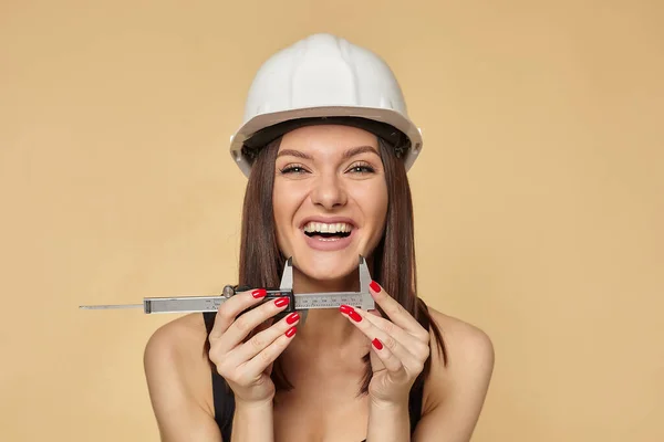 戴着白色硬礼帽戴着建筑用防护面具的女建筑工人拿着口径手枪 测量微笑的大小 — 图库照片