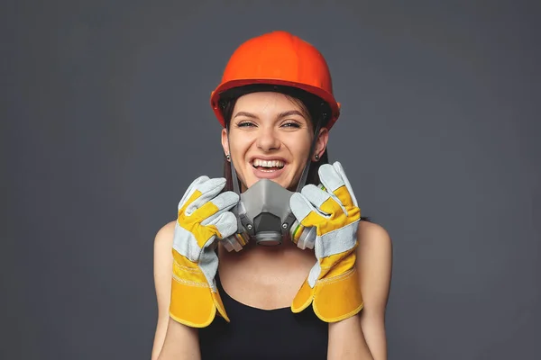 Construction girl in orange hard hat and protective construction mask, for heavy work where you need protection from inhaling harmful gases and sprayed particles in the air