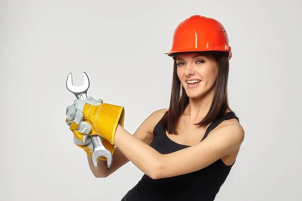 戴着橙色头盔的建筑女孩拿着扳手在扭动可想而知的螺栓时抛出 — 图库照片