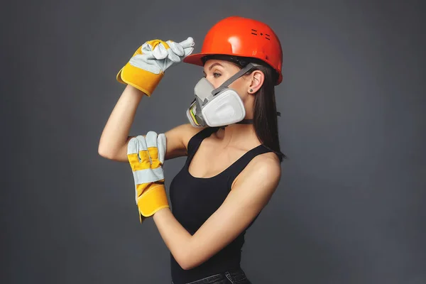 Construction girl in an orange hard hat and protective construction mask, for heavy work where you need protection from inhaling harmful gases and sprayed particles in the air. the concept of advertising