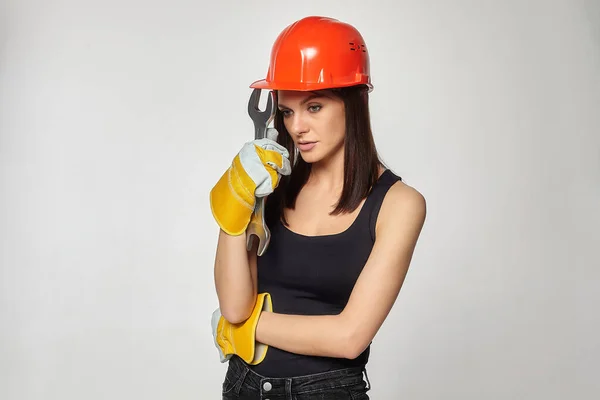 戴着橙色头盔的漂亮女人 手里拿着扳手 在工作时抛锚 拧一个假想的螺栓 — 图库照片