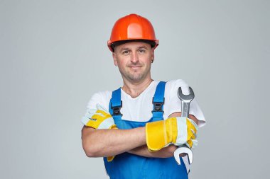 İnşaat kaskı takan yetişkin bir adamın elinde anahtar var. İnşaat hizmetleri kavramı