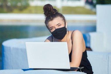 Maskeli güzel bir kız dizüstü bilgisayarla şehirde dolaşıyor. Elinde dizüstü bilgisayarla müzik dinliyorsun..