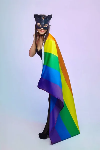 a woman in a cat mask holds a rainbow flag.