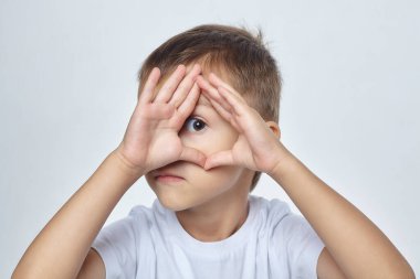 Küçük çocuk parmaklarının arasından ileriye bakıyor..