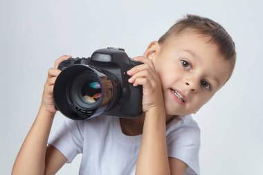 Stüdyoda beyaz arka planda fotoğraf makinesiyle poz veren sevimli çocuk.