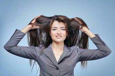 Çekici kız kameranın önünde şakacı bir şekilde poz veriyor. Stüdyoda mavi arka planda yakın plan portresi