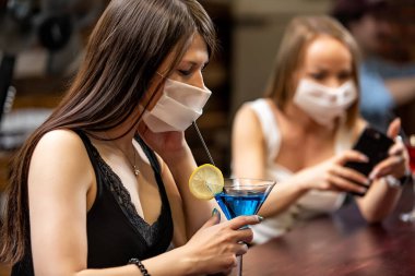 Tıp maskeli kızlar barda sohbet ediyorlar. Tıp maskeli kızlar barda konuşuyorlar. Maskeli kızlar kokteyl içer.