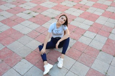 Genç, neşeli, genç bir bayan. Kırsalda oturuyor. Şık yaz kıyafetleri giyiyor. Çanta. Sıcak akşam renkleri. Güneş