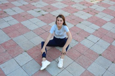 Genç, neşeli, genç bir bayan. Kırsalda oturuyor. Şık yaz kıyafetleri giyiyor. Çanta. Sıcak akşam renkleri. Güneş