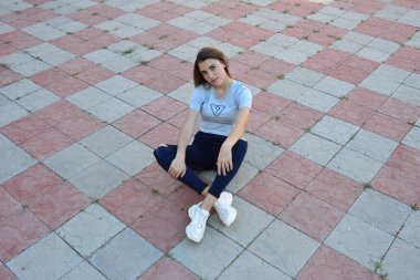 Genç, neşeli, genç bir bayan. Kırsalda oturuyor. Şık yaz kıyafetleri giyiyor. Çanta. Sıcak akşam renkleri. Güneş