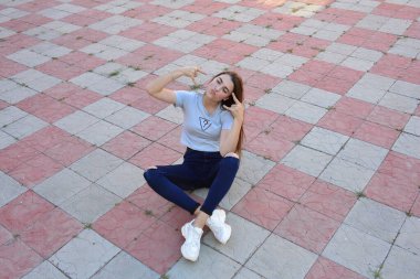 Genç, neşeli, genç bir bayan. Kırsalda oturuyor. Şık yaz kıyafetleri giyiyor. Çanta. Sıcak akşam renkleri. Güneş