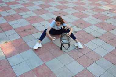 Genç, neşeli, genç bir bayan. Kırsalda oturuyor. Şık yaz kıyafetleri giyiyor. Çanta. Sıcak akşam renkleri. Güneş