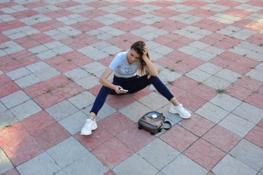 Genç, neşeli, genç bir bayan. Kırsalda oturuyor. Şık yaz kıyafetleri giyiyor. Çanta. Sıcak akşam renkleri. Güneş