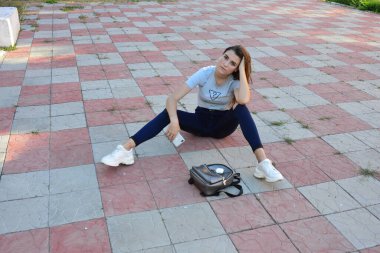 Genç, neşeli, genç bir bayan. Kırsalda oturuyor. Şık yaz kıyafetleri giyiyor. Çanta. Sıcak akşam renkleri. Güneş