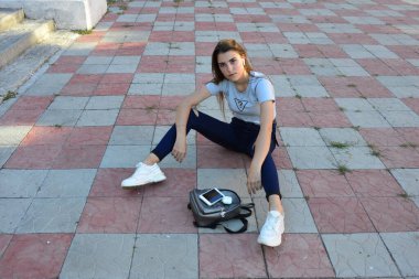 Genç, neşeli, genç bir bayan. Kırsalda oturuyor. Şık yaz kıyafetleri giyiyor. Çanta. Sıcak akşam renkleri. Güneş