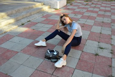 Genç, neşeli, genç bir bayan. Kırsalda oturuyor. Şık yaz kıyafetleri giyiyor. Çanta. Sıcak akşam renkleri. Güneş