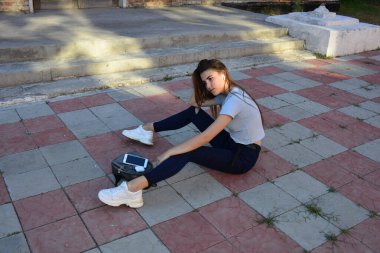 Genç, neşeli, genç bir bayan. Kırsalda oturuyor. Şık yaz kıyafetleri giyiyor. Çanta. Sıcak akşam renkleri. Güneş