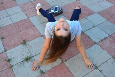 Genç, neşeli, genç bir bayan. Kırsalda oturuyor. Şık yaz kıyafetleri giyiyor. Çanta. Sıcak akşam renkleri. Güneş