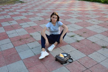 Genç, neşeli, genç bir bayan. Kırsalda oturuyor. Şık yaz kıyafetleri giyiyor. Çanta. Sıcak akşam renkleri. Güneş