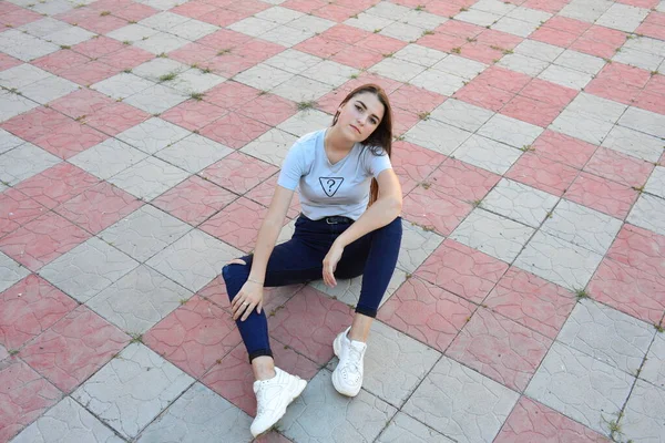 Genç, neşeli, genç bir bayan. Kırsalda oturuyor. Şık yaz kıyafetleri giyiyor. Çanta. Sıcak akşam renkleri. Güneş