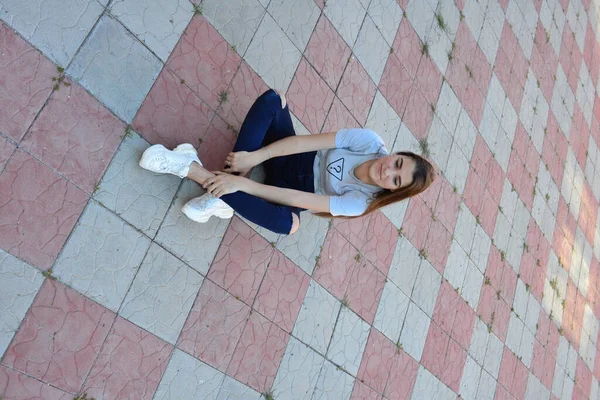 Genç, neşeli, genç bir bayan. Kırsalda oturuyor. Şık yaz kıyafetleri giyiyor. Çanta. Sıcak akşam renkleri. Güneş