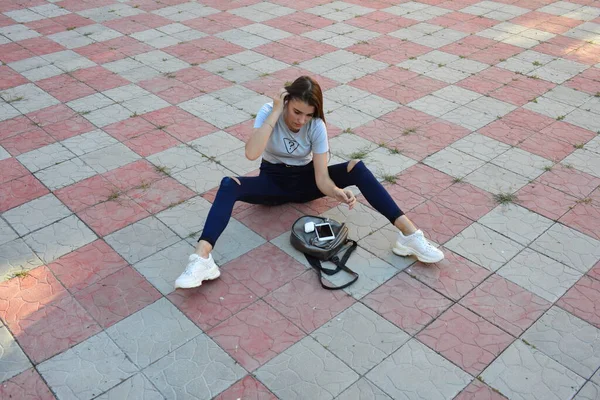 Genç, neşeli, genç bir bayan. Kırsalda oturuyor. Şık yaz kıyafetleri giyiyor. Çanta. Sıcak akşam renkleri. Güneş