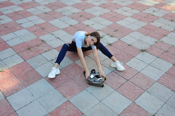 Genç, neşeli, genç bir bayan. Kırsalda oturuyor. Şık yaz kıyafetleri giyiyor. Çanta. Sıcak akşam renkleri. Güneş