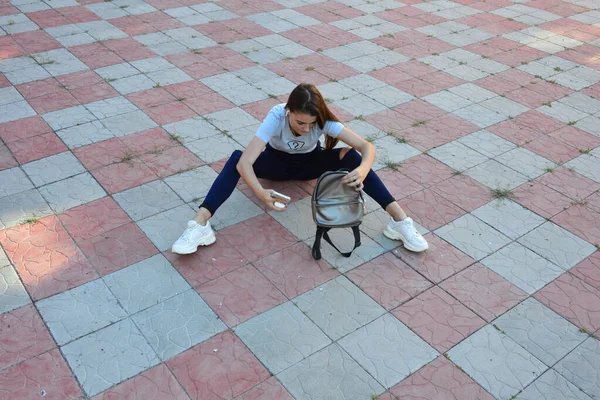 Genç, neşeli, genç bir bayan. Kırsalda oturuyor. Şık yaz kıyafetleri giyiyor. Çanta. Sıcak akşam renkleri. Güneş