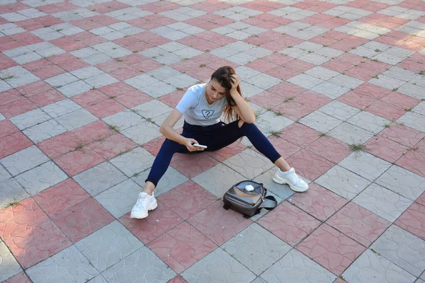 Genç, neşeli, genç bir bayan. Kırsalda oturuyor. Şık yaz kıyafetleri giyiyor. Çanta. Sıcak akşam renkleri. Güneş