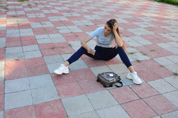 Genç, neşeli, genç bir bayan. Kırsalda oturuyor. Şık yaz kıyafetleri giyiyor. Çanta. Sıcak akşam renkleri. Güneş