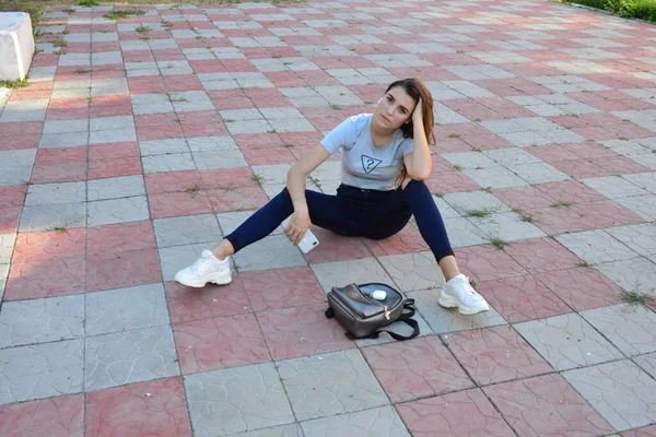 Genç, neşeli, genç bir bayan. Kırsalda oturuyor. Şık yaz kıyafetleri giyiyor. Çanta. Sıcak akşam renkleri. Güneş