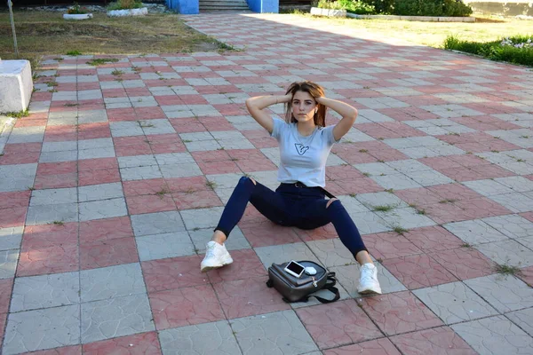 Genç, neşeli, genç bir bayan. Kırsalda oturuyor. Şık yaz kıyafetleri giyiyor. Çanta. Sıcak akşam renkleri. Güneş