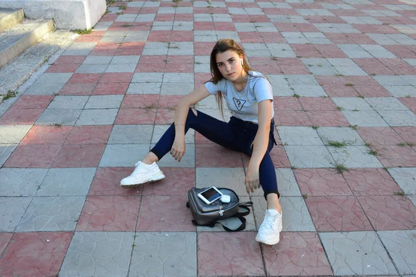 Genç, neşeli, genç bir bayan. Kırsalda oturuyor. Şık yaz kıyafetleri giyiyor. Çanta. Sıcak akşam renkleri. Güneş