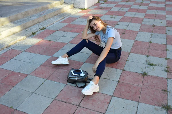 Genç, neşeli, genç bir bayan. Kırsalda oturuyor. Şık yaz kıyafetleri giyiyor. Çanta. Sıcak akşam renkleri. Güneş