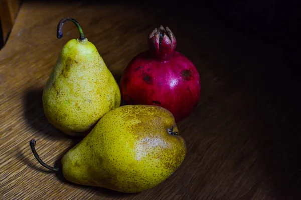 Um par de peras amarelas orgânicas maduras frescas e uma romã na mesa de madeira. Foco seletivo. — Fotografia de Stock