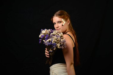 Stüdyoda siyah üzerine yakın plan yapılmış güzel bir kadın yüzü. Çiçek buketi.