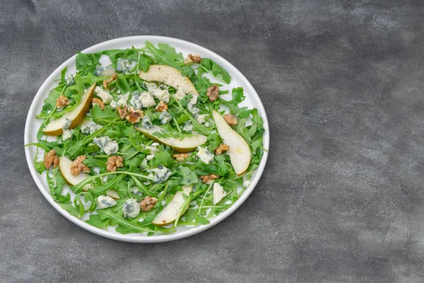 Vegetarian salad with arugula leaves, pear, blue cheese, and walnuts.