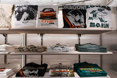 Taşkent, Özbekistan, 18 Ağustos 2025: Otomotiv, sokak giyimi ve perakende sergilenen resimli tasarımların yer aldığı raflarda düzgünce düzenlenmiş grafiksel tişörtler