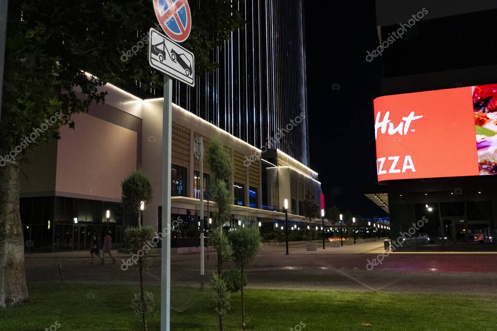 Tashkent, Uzbekistan, August 18, 2025: Vibrant nighttime urban view featuring a modern building with illuminated Pizza Hut billboard, streetlights, and pedestrians in a lively city setting