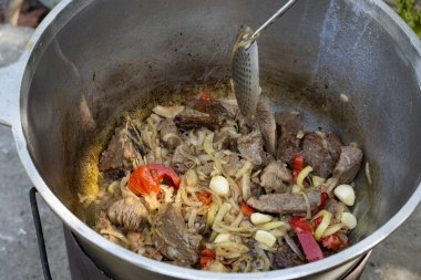 Bir kazanda yanan et, soğan, sarımsak ve dolma biber parçaları. Geleneksel açık hava yemek sahnesi, kırsal ve iştah açıcı.