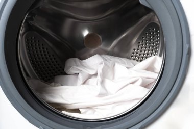 Çamaşır makinesinin önü beyaz çamaşırlarla dolu. Çamaşır bakımını, alet tasarımını ve ev işlerini gösteren bir varil.