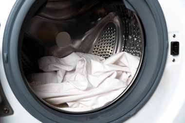 Çamaşır makinesinin önü beyaz çamaşırlarla dolu. Çamaşır bakımını, alet tasarımını ve ev işlerini gösteren bir varil.