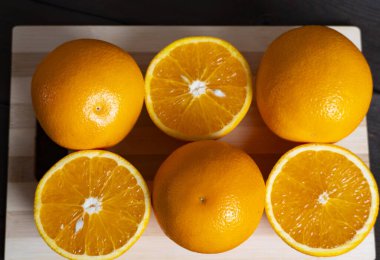 Ahşap bir kesme tahtasının üzerinde tam ve yarıya indirilmiş olgun portakallar. C vitamini açısından zengin taze narenciye, beslenme, sağlıklı yaşam tarzı, diyet ve gıda kavramları için mükemmel.