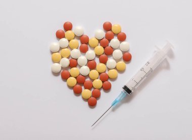 Bir şırınga ve beyaza izole edilmiş kalp şeklinde sarı, beyaz ve kırmızı haplar. 