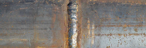Closeup of a solidified slag on a welded butt joint. Two metal plates welded together as a background