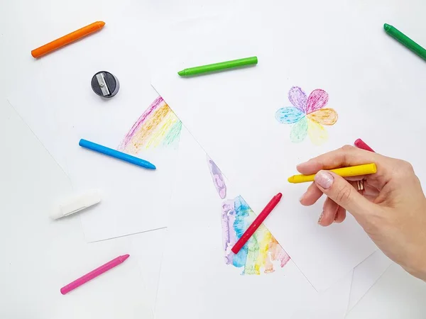 Lápis de cera colorida em papel branco. A mão segura um lápis e desenha uma flor com pétalas coloridas . — Fotografia de Stock